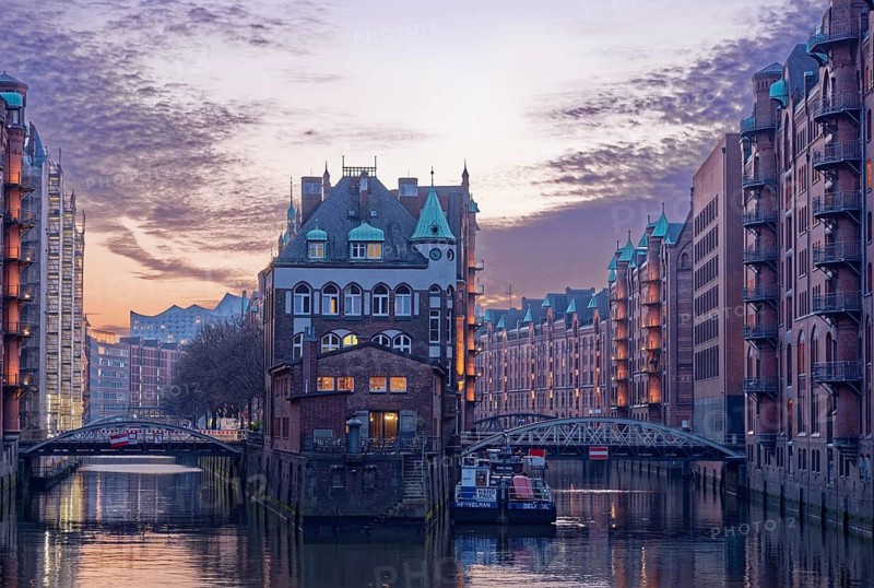 The moated castle in Hamburg's Speicherstadt between the Holländischbrookfleet and the Wandrahmfleet with the bridges of the Servant Row. At dusk, windows are illuminated. Speicherstadt, Hamburg, Germany