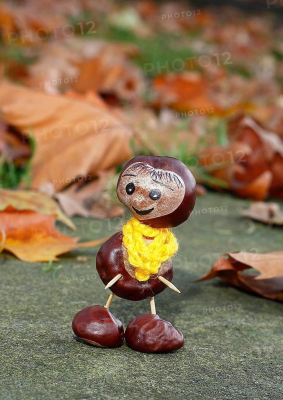 Funny chestnut figure with yellow scarf on a wall in autumn leaves, North Rhine-Westphalia, Germany