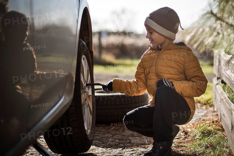 Young boy turns the spanner during changing the wheel in the car