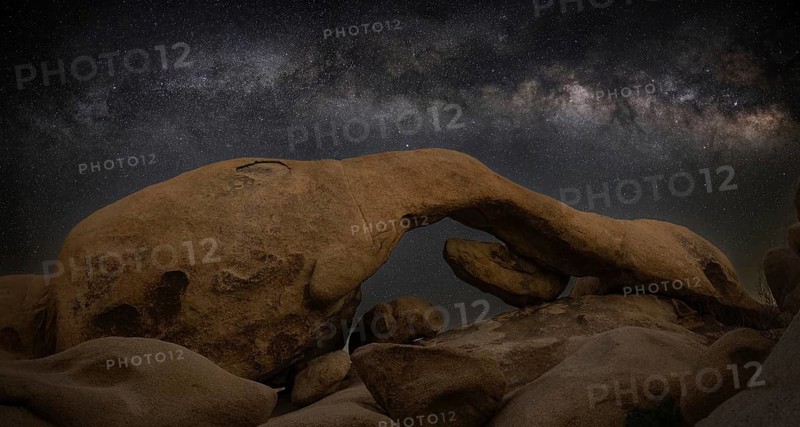 A stunning long exposure of Joshua Tree National Park's vast desert, showcasing the Milky Way arching above rock formations