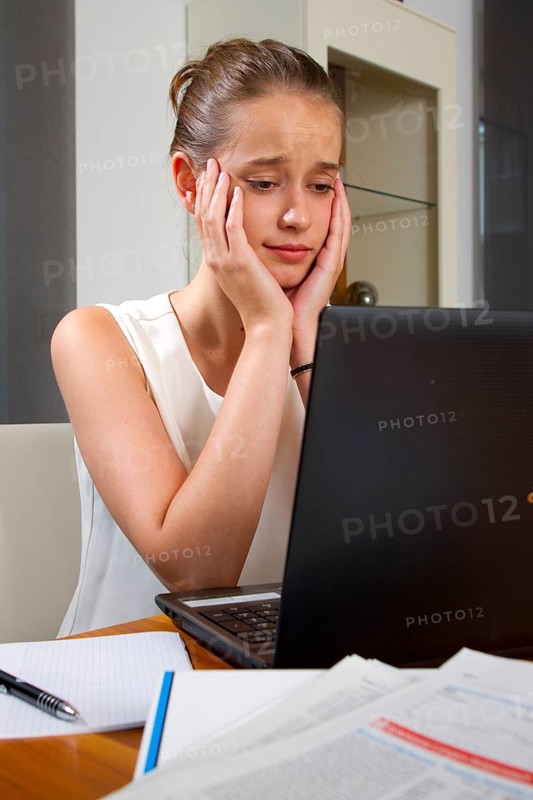 A twenty-year-old young woman sits disappointed in front of her laptop, computer