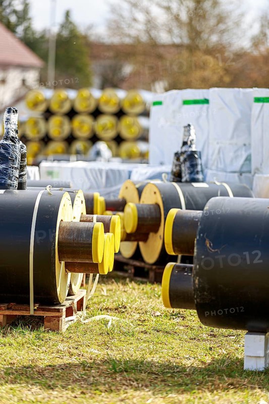 Stacked district heating pipes and district heating pipes with yellow ends lie in a pile in a meadow