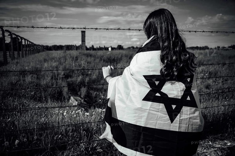 Jewish girl with Israeli flag by the fence of the concentration camp