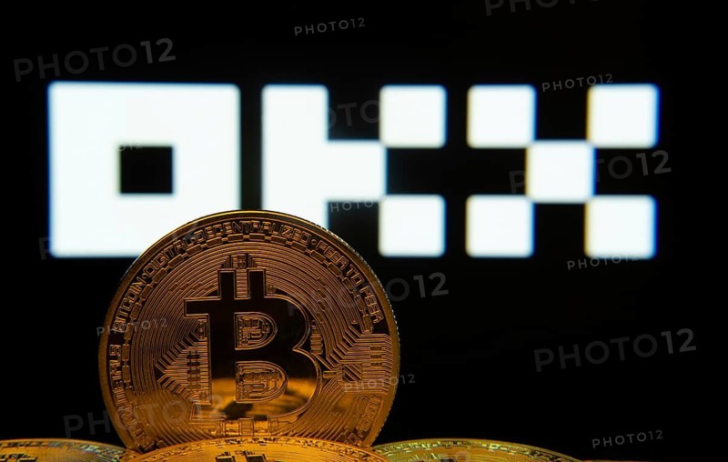 Dhaka, Bangladesh- 04 April 2025: Close-up of Bitcoin coins with the OKX logo visible on a screen in the background