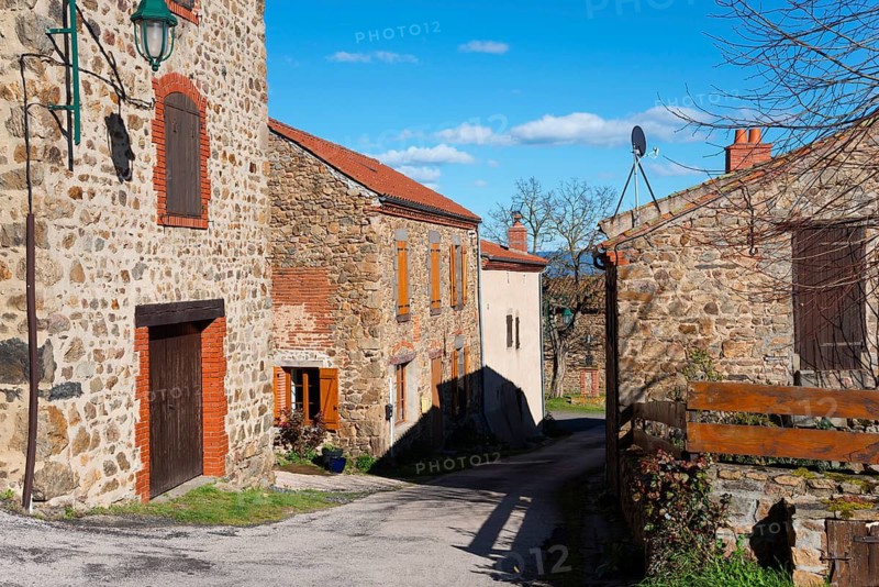 Eine ruhige Dorfstraße mit steinernen Häusern und Fensterläden unter einem sonnigen, blauen Himmel, Léotoing, Leotoing, Haute-Loire, Auvergne-Rhône-Alpes, Auvergne-Rhone-Alpes, Frankreich