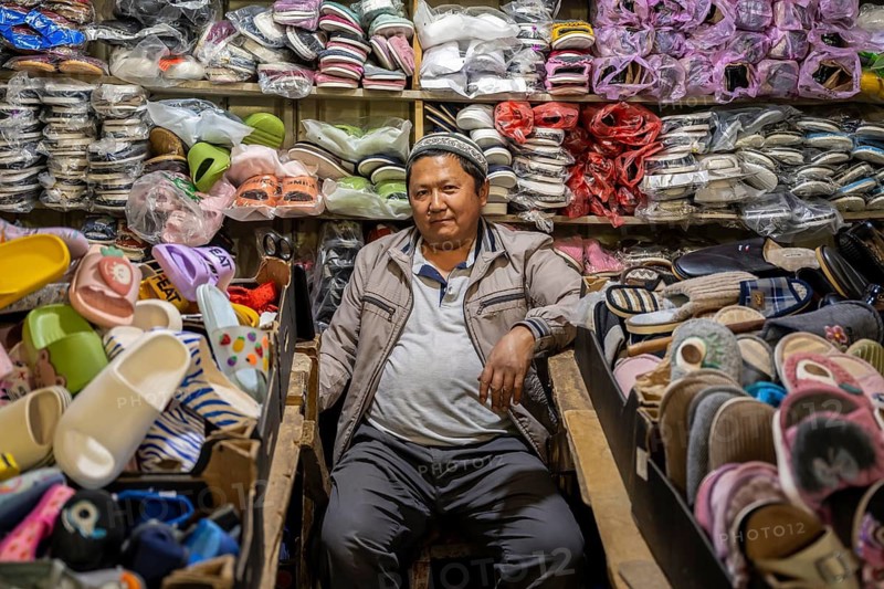Man amidst many shoes and clothes, stall at the Osh Bazaar, Bishkek, Kyrgyzstan