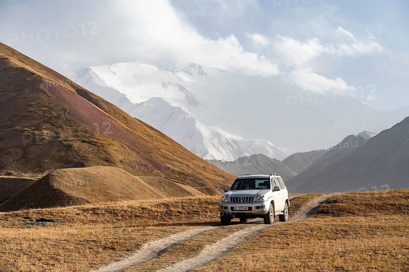 Off-road vehicle on a track between yellow meadows, glaciated high mountain peaks in the background, Lenin Peak, Trans Alay Mountains, Pamir Mountains, Osh Province, Kyrgyzstan