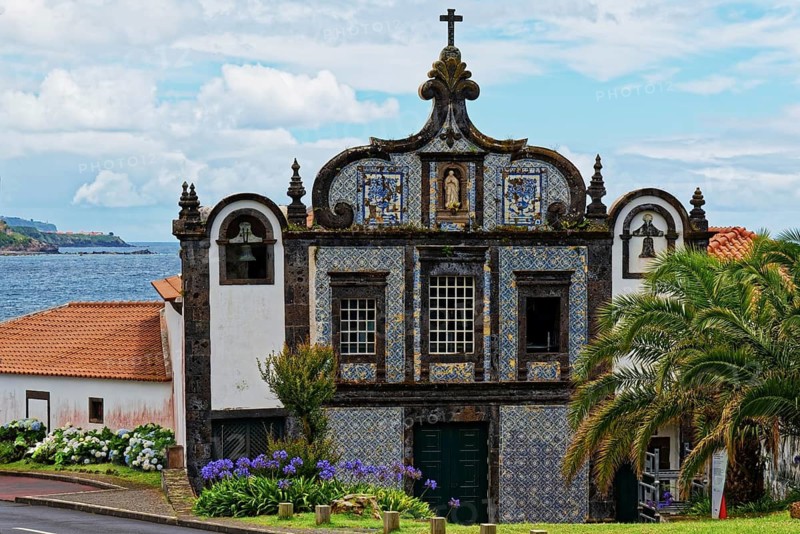Historic church Convent of Caloura on the coast with blue and white tiles and sea view, surrounded by flowers and a palm tree, fishing village Caloura, Ribeira Chã, Sao Miguel Island, Azores, Portugal
