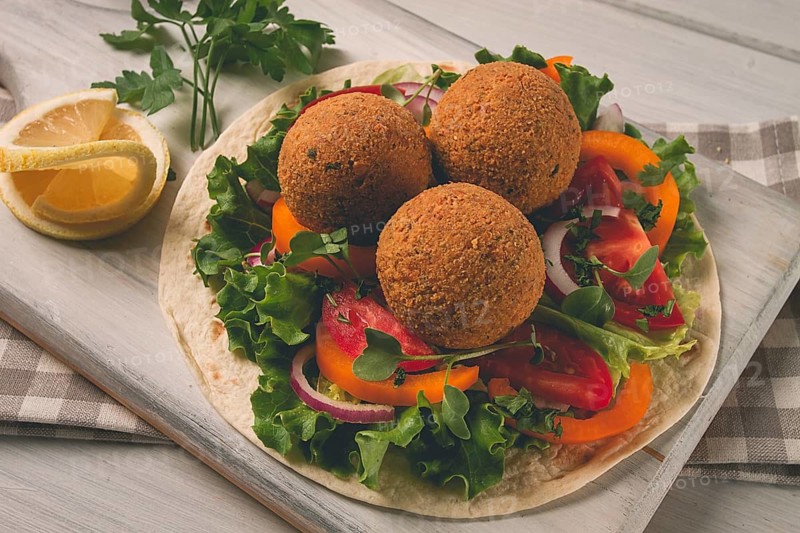 Tortillas, wrapped falafel balls, with fresh vegetables, vegetarian healthy food, on a wooden white background, no people, selective focus.