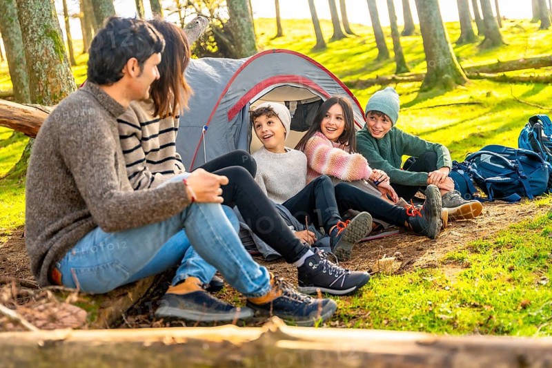 Parents talking with their three children sitting on camping tent enjoying a weekend trekking together