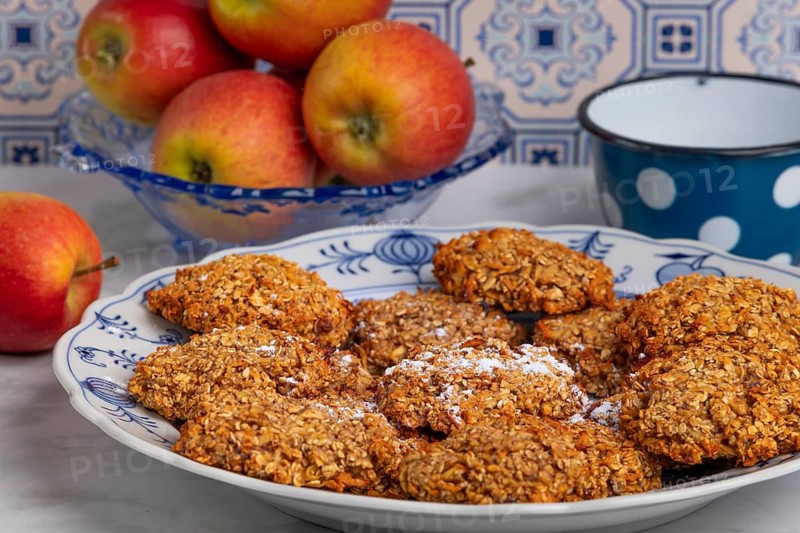 Freshly baked oat biscuits on a plate with apples in the background