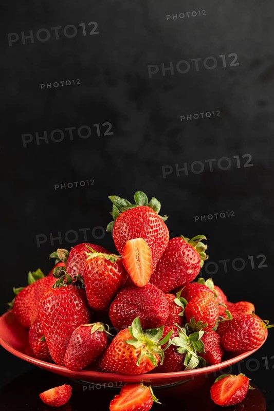 A pile of fresh red strawberries on a red plate against a black background