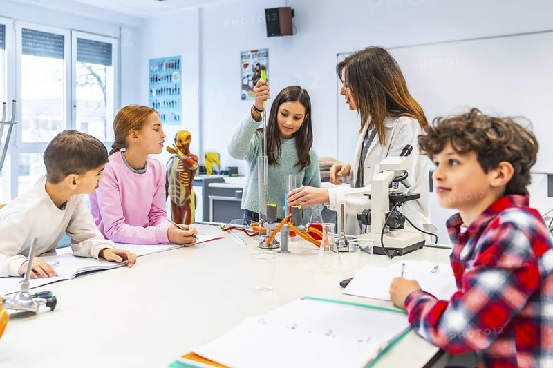 Elementary school students learning science and performing experiments with test tubes and microscope during a chemistry lesson with their teacher