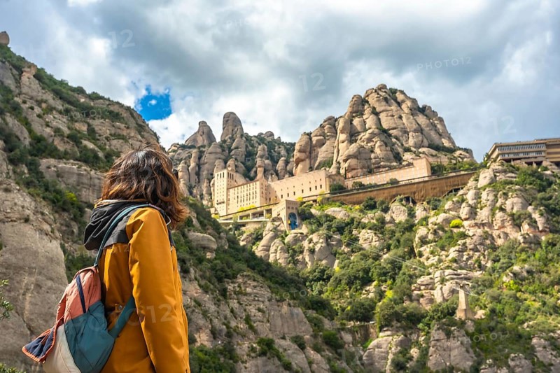 Hiker admiring santa maria de montserrat abbey, a benedictine monastery located on the mountain of montserrat, in monistrol de montserrat, catalonia, spain