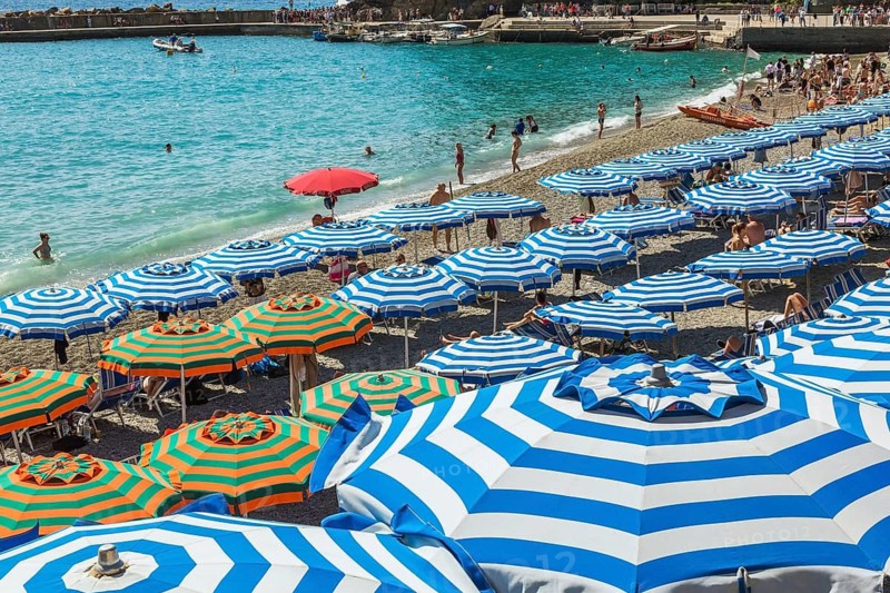 Beach with bathers, tourists and blue parasols in late summer, Monterosso village, Cinque Terre, La Spezia province, Italy