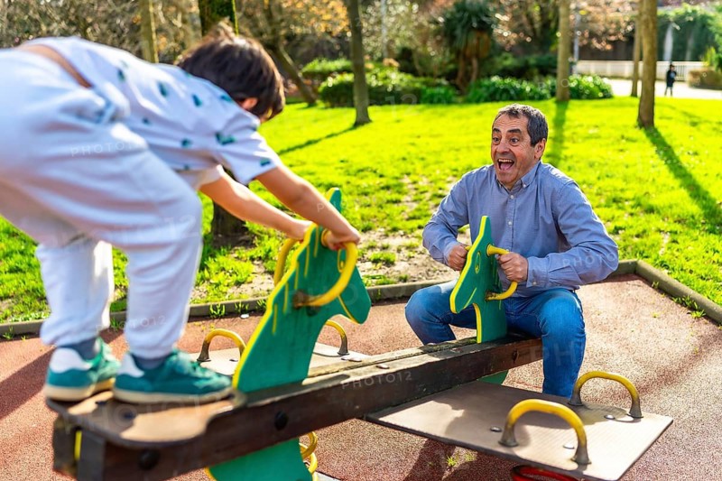 Grandfather and grandson enjoying leisure time together, playing on a seesaw in a park, promoting family bonding and intergenerational connection