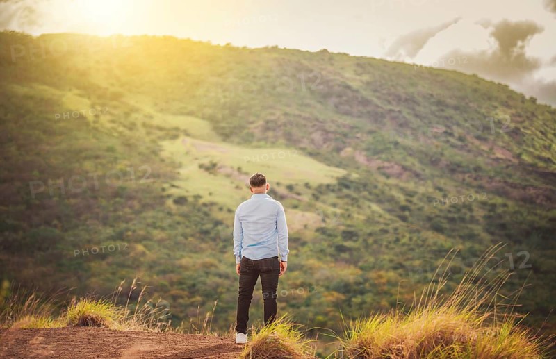 Back view of lonely man on a hill at sunset. Rear view of a lonely man on top of a hill looking at the horizon