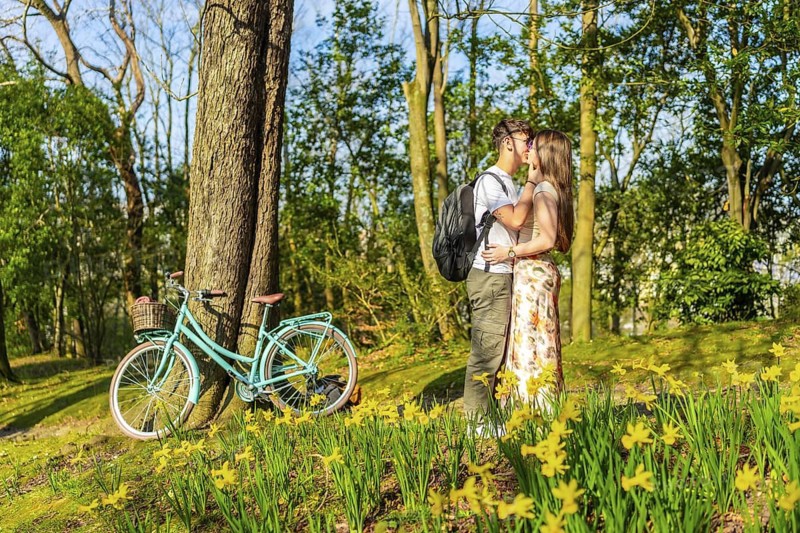 Romantic couple kissing in a spring park with a bicycle leaning against a tree and daffodils in the foreground