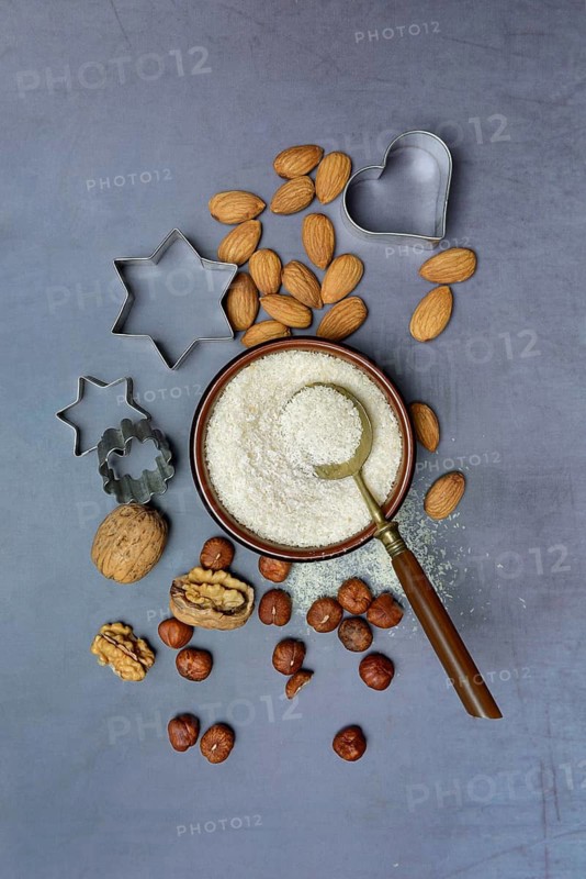 Grated coconut in a bowl and spoon, various nuts and cookie cutters