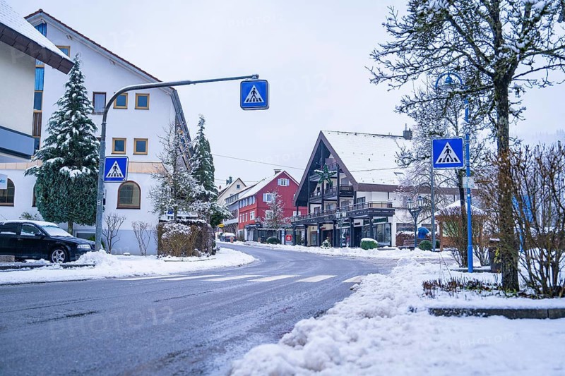 Snow-covered street in a village surrounded by traditional houses and road signs, Enzklösterle, Calw district, Black Forest, Germany
