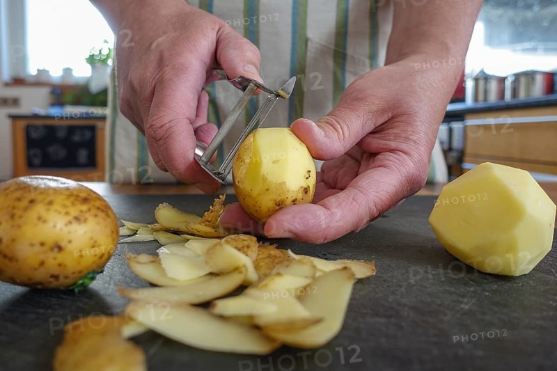 Swabian cuisine, preparation of potato salad, peeling raw potatoes, savoury, salty, typical Swabian, typical Christmas dinner, quick cuisine for Christmas Eve, home cooking, traditional cuisine, men's hands, asparagus peeler, vegetable peeler, cutting board, food photography, studio, Germany