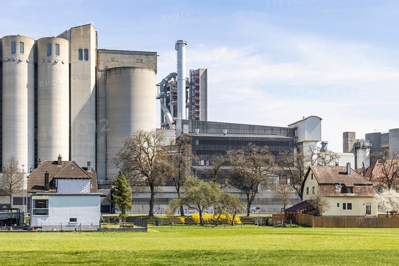 SCHWENK cement works in Heidenheim-Mergelstetten. In front, residential buildings with an idyllic garden as a contrast to the concrete towers. Heidenheim, Baden-Württemberg, Germany