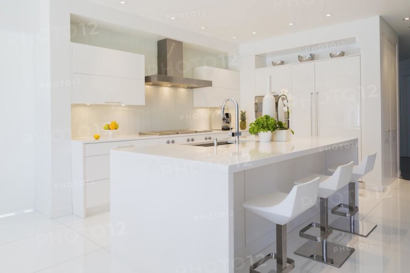 Modern kitchen with white Italian lacquered island and chrome bar stools, cabinets and countertops inside a luxurious residential home, Quebec, Canada