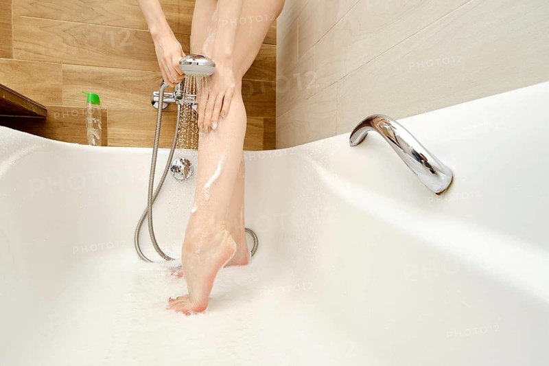 Closeup view of unrecognizable woman washes away soap suds while standing in the bathroom