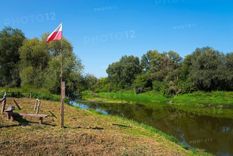 Riverbank with Polish flag and benches, surrounded by trees under a clear sky, bow River, border with Ukraine, Bereznica, Bereznica, Dorohusk, Horodlo, Horodlo, Hrubieszowski Voivodeship, Lublin Voivodeship, Poland