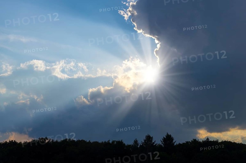 Rain clouds with sun shining through, sunbeams, blue sky, forest