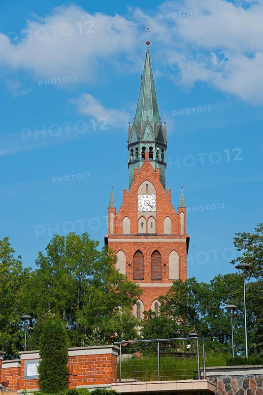 High red-brick church tower with clock, surrounded by green trees under a bright blue sky, Sacred Heart Church, Elk, Elk, Lyck, Warmia-Masuria, Poland