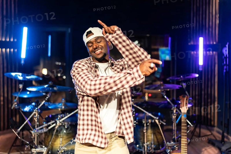 Young male music artist dancing urban style in professional recording studio with instruments in background