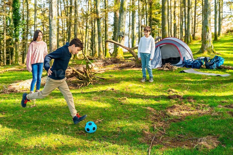 Caucasian young members of a family playing football in the forest together enjoying camping in the nature