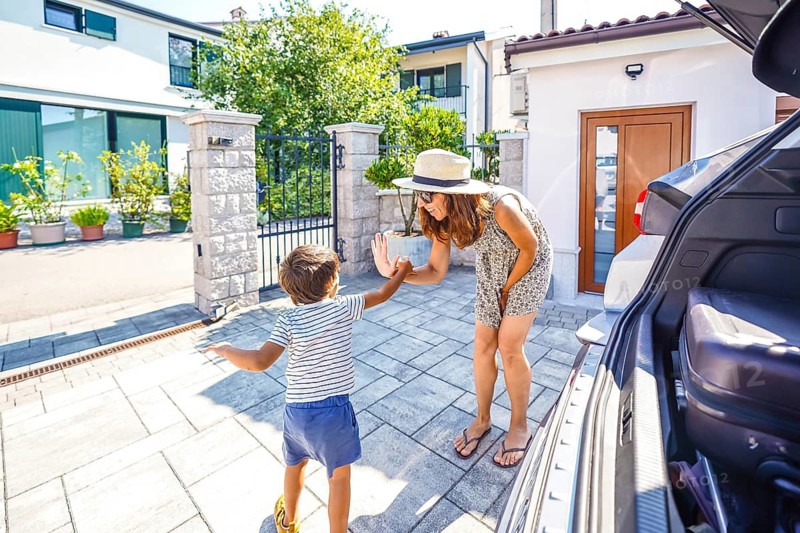 Happy mother giving high five to her son in front of their house before leaving for summer vacation with their car