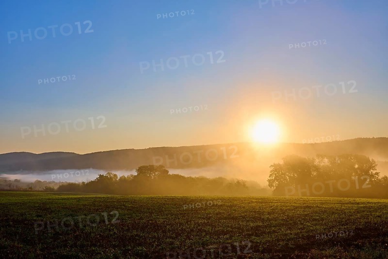 Sunrise over a foggy cornfield with forest, in the background hills under a clear sky, Großheubach, Miltenberg, Spessart, Bavaria, Germany