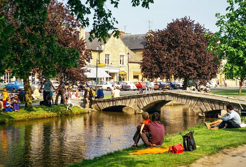 Menschen am Flussufer sitzend, River Windrush, Bourton on the Water, Gloucestershire, England, UK Mai 1973