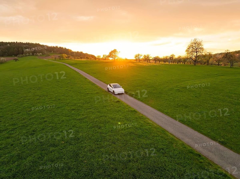 A car drives on a long road through a green landscape at sunset, Tesla New Model Y, Germany
