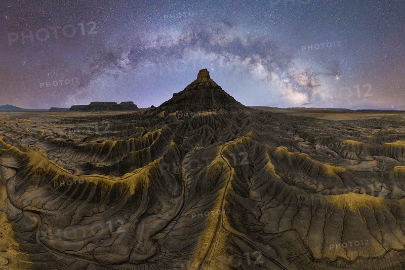 Stunning view of the Milky Way over a sandstone desert in Utah, USA. The sky sparkles with countless stars, illuminating the intricate patterns of the rugged terrain below