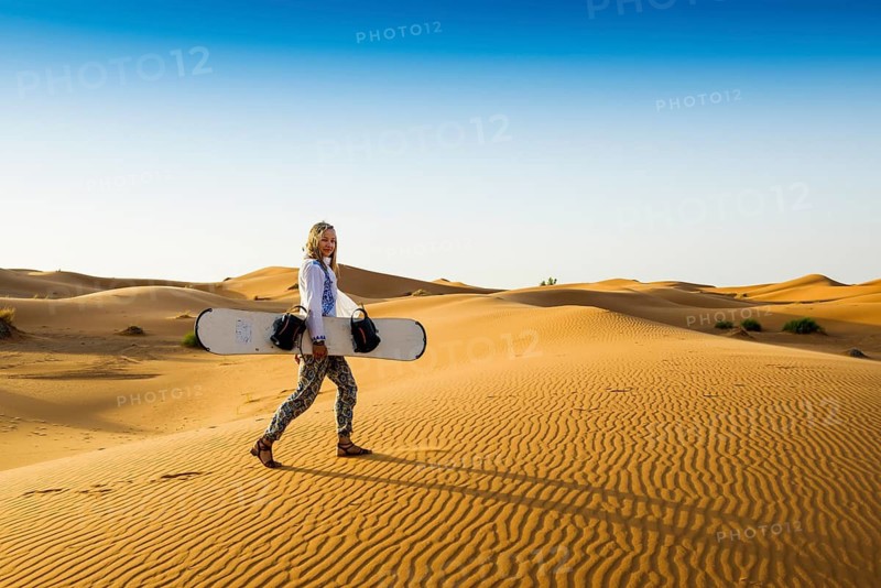 Young woman with snowboard in the sand dunes, near Merzouga, Meknès-Tafilalet region, Erg Chebbi, northern Sahara, Morocco