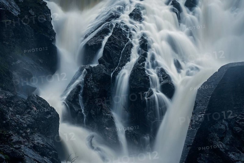 A mesmerizing long exposure photograph capturing the smooth, flowing water cascading over rugged rocks at Presa del Villar, Madrid, creating a tranquil and ethereal scene