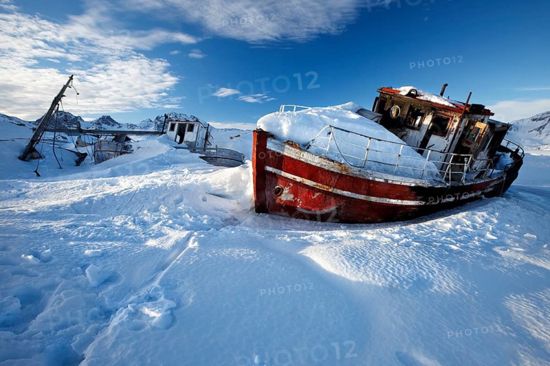 Kong Oscar Havn. Tasiilaq, East Greenland – a fishing boats lies frozen in the harbor, trapped by winter ice and snow