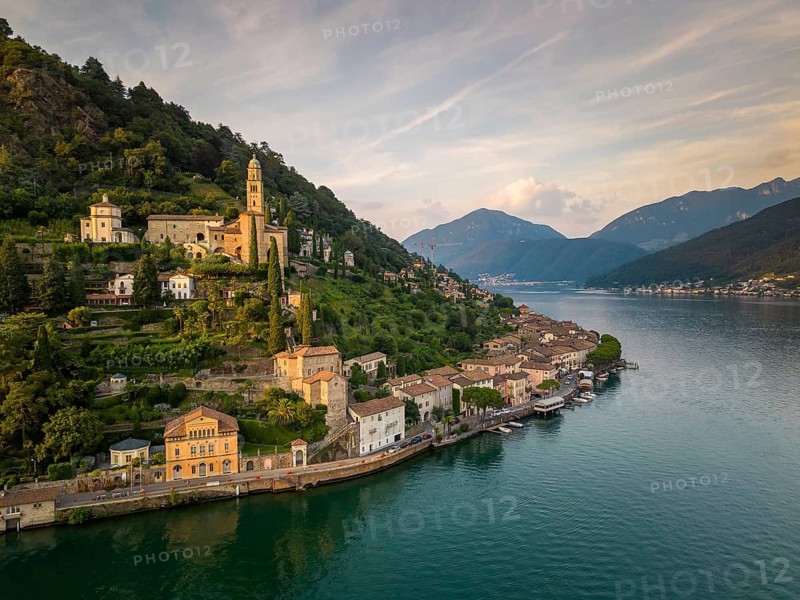 Captivating evening view of Morcote, set along the tranquil shores of Lake Lugano in Switzerland. The picturesque village and its lush surroundings create a serene, idyllic atmosphere