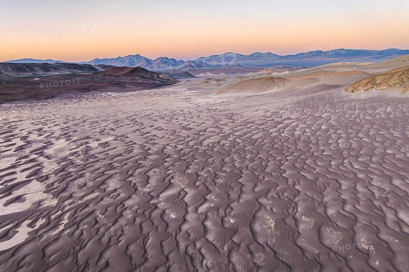 Vast pumice field under a clear sky in Catamarca, Argentina, showcasing textured volcanic rock formations. Distant mountains create a serene, ethereal landscape