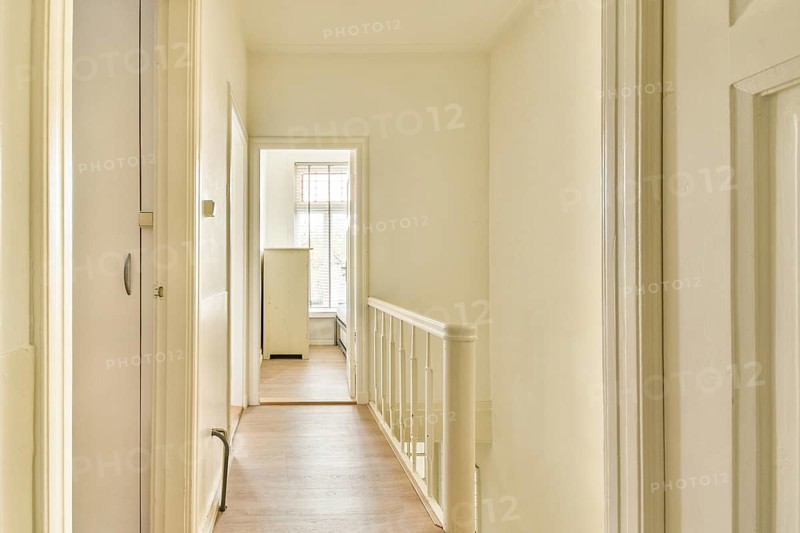 A well-lit hallway features white walls and wooden flooring, creating an inviting and spacious atmosphere. The light streaming in enhances its brightness