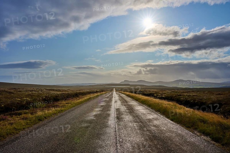 Sun rays penetrate the clouds over a long road that crosses a vast landscape, Tongue, Lairg, Scotland, United Kingdom, Great Britain