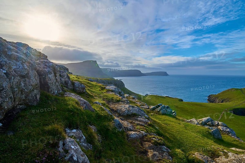 The sun breaks through the clouds over green cliffs and blue sea, Waterstein Head, Waterstein, Isle of Skye, Scotland, United Kingdom, Great Britain