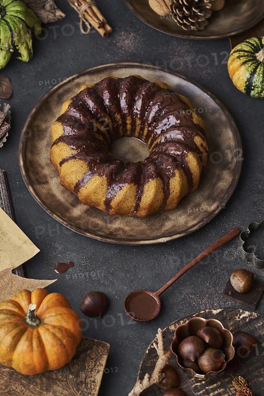 From above tasty appetizing pumpkin cake with chocolate cream on table decorated with autumn vegetables