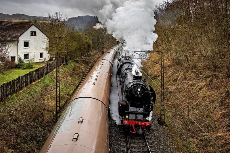 A steaming locomotive travels along a house and forest on winding tracks, historic steam locomotive ride between Bebra and Sontra