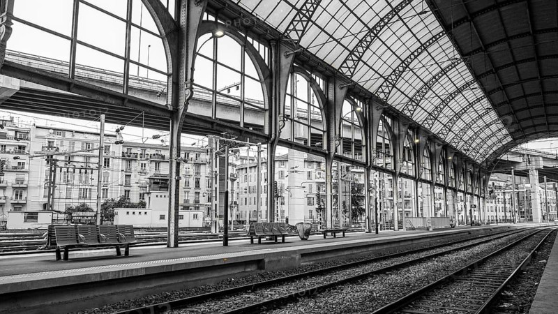 Monochrome image capturing the stunning architecture of a train station in Nice, France, showcasing sweeping arches and intricate metalwork