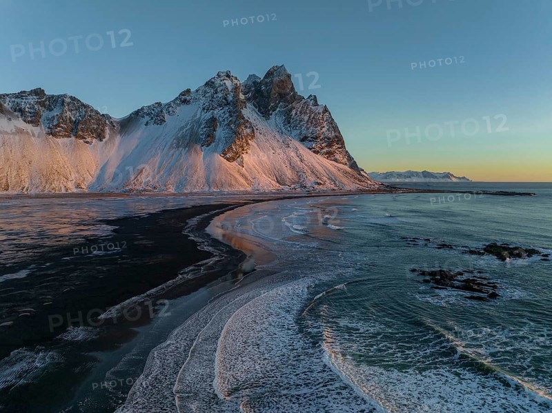 A Stunning view of Stokksnes Mountain, with its snow-covered peaks and the unique black sand beach. The serene scene captures the essence of Iceland's natural beauty